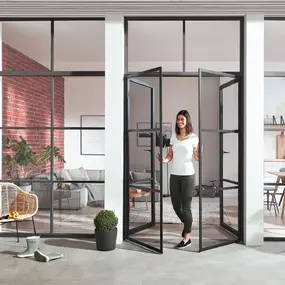 Frau öffnet moderne schwarze Glasdrehtür zwischen Wohnzimmer und Esszimmer mit Pflanzen.
