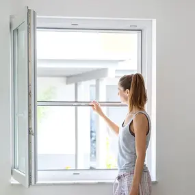 Frau installiert Insektenschutz am Fenster für effektiven Schutz vor Mücken und Insekten.