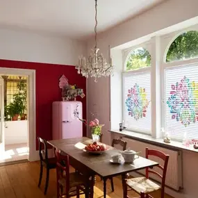 Heller, gemütlicher Essbereich mit Holztisch, buntem Kühlschrank und großen Fenstern.