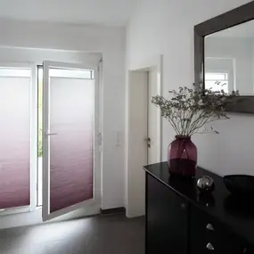 Heller Flur mit Plissees an Terrassentüren, Spiegel, Dekovase und modernem Sideboard.