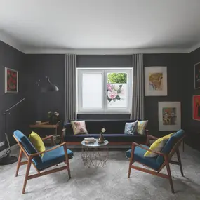 Modernes Wohnzimmer mit grauen Wänden, bunten Bildern, blauen Sesseln und Dekokissen.