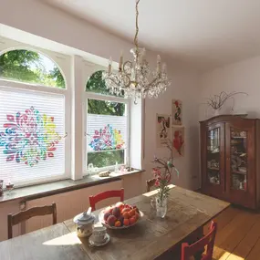 Heller Esszimmerraum mit Holztisch, bunten Plissees am Fenster und Kronleuchter.