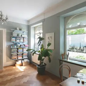 Helles Arbeitszimmer mit Parkett, Bücherregal, Zimmerpflanze und großem Fenster.