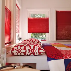 Modernes Schlafzimmer mit roten Jalousien und farbenfroher Bettwäsche im Tageslicht.