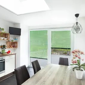 Moderne, helle Küche mit Esstisch, grünen Jalousien und dekorativen Pflanzen am Fenster.