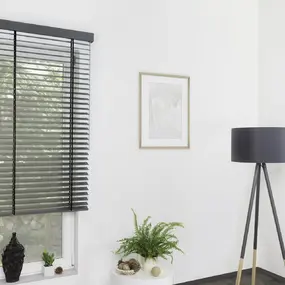 Modernes Wohnzimmer mit schwarzen Jalousien, Stehlampe und dekorativen Zimmerpflanzen.