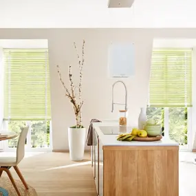 Helle, moderne Wohnküche mit Holzinsel, Essbereich und grünen Jalousien am Fenster.