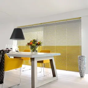 Moderner Essbereich mit gelben Stühlen, Holztisch und gelb-grauen Jalousien am Fenster.