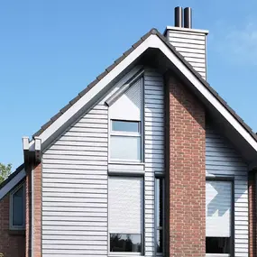 Modernes Einfamilienhaus mit Klinkerfassade, Rollläden und Satteldach bei Sonnenschein.