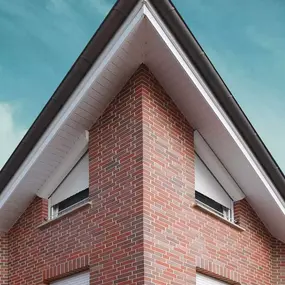 Backstein-Fassade eines modernen Einfamilienhauses mit Satteldach und weißen Rollläden.