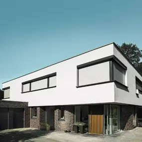 Modernes Einfamilienhaus mit Flachdach, großen Fenstern und Rollläden im Vorgarten.