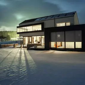 Modernes Einfamilienhaus mit großen Fenstern im verschneiten Garten bei Nacht.