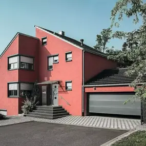 Modernes Einfamilienhaus mit roter Fassade, Garage und gepflasterter Einfahrt.