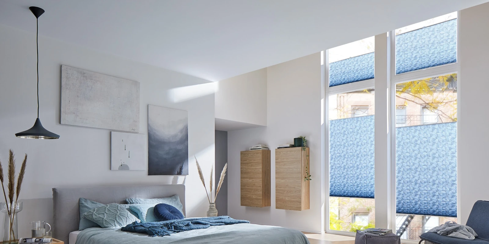 Modernes Schlafzimmer mit großen Fenstern und blauen Plissees als Sichtschutz.