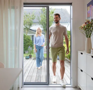 Paar betritt durch Schiebetür das Haus, modernes Wohnen, Terrasse im Hintergrund