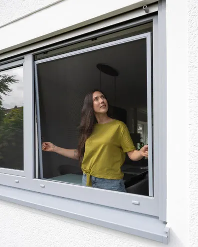 Frau öffnet Insektenschutz am Fenster, Fliegengitter für Mückenschutz zuhause
